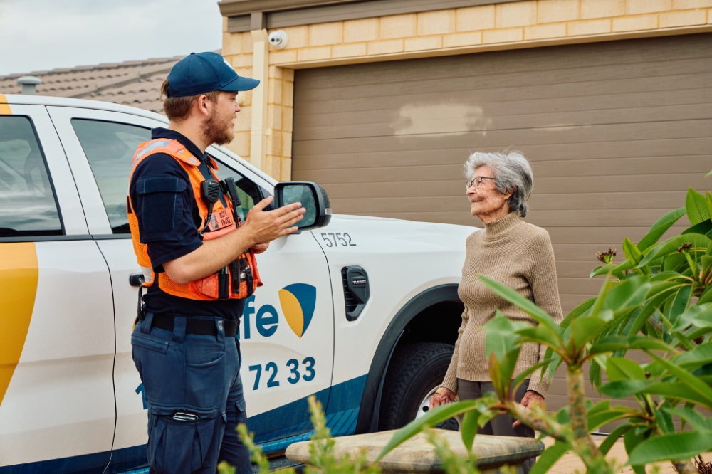 CoSafe officer speaking with a resident outside her home, in front of a CoSafe patrol vehicle