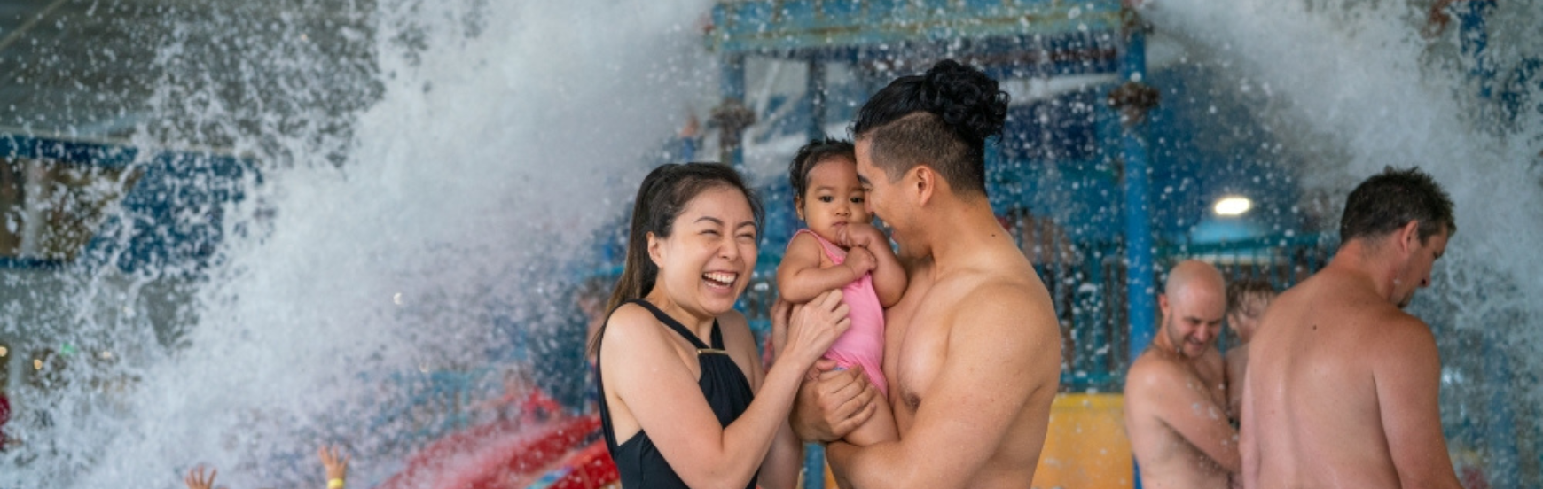 A family standing under the water bucket in the Cockburn ARC indoor pool, laughing